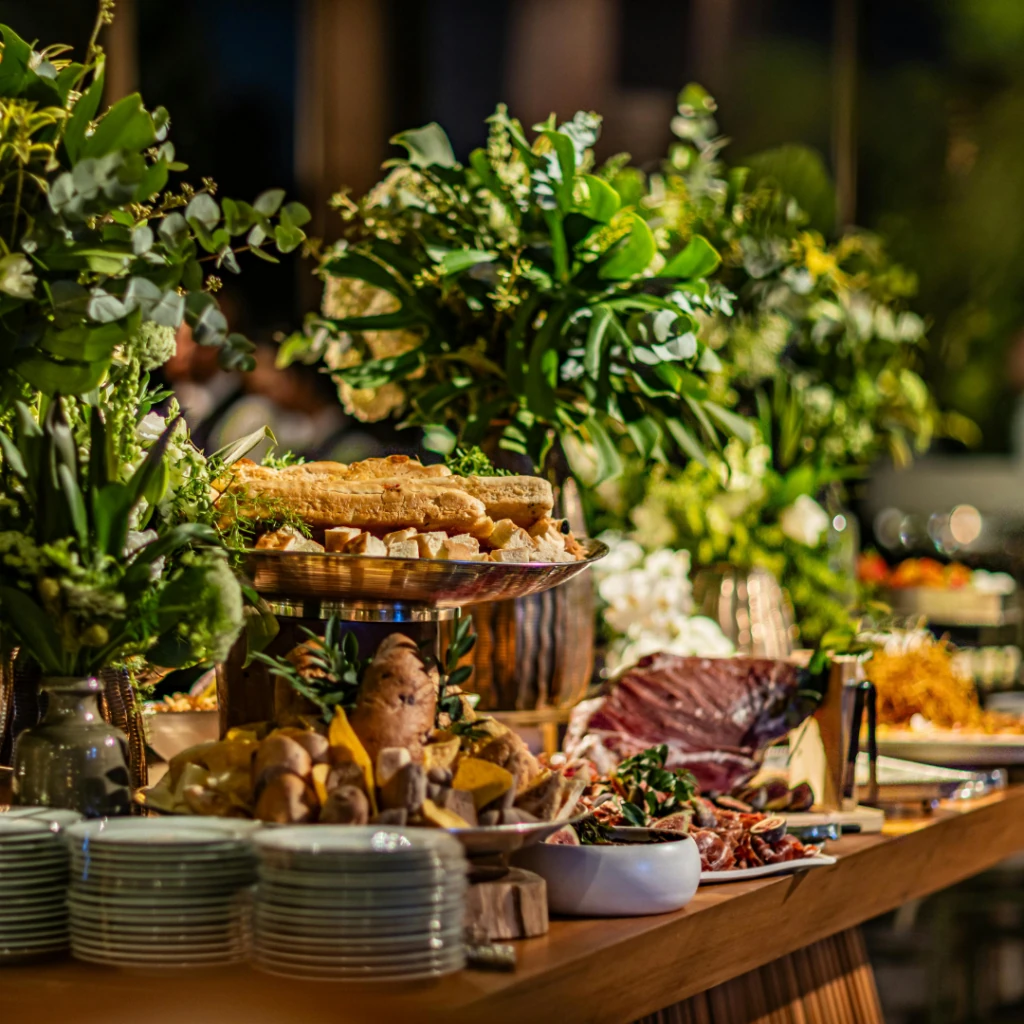Mesa de buffet com pães, frios e arranjos de folhagem