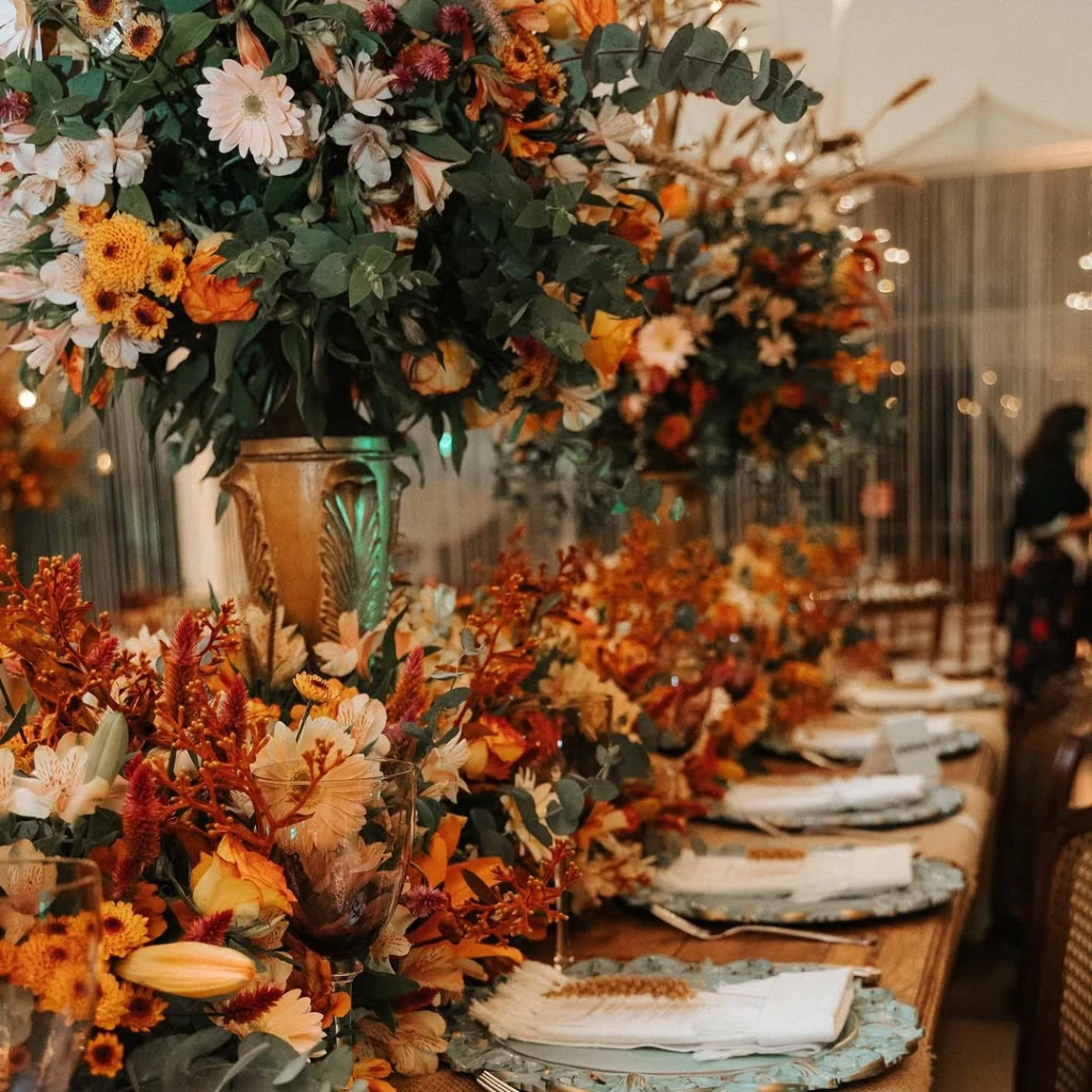 Mesa posta com arranjos de flores naturais em tons laranja e branco
